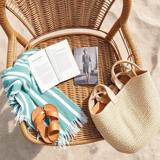 Wicker chair flat lay with sandals, book, towel, and beach bag